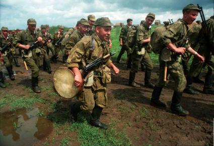 Колонна солдат в полной боевой выкладке идет по грязной разбитой дороге. Солдат на переднем плане несет на боку барабан.