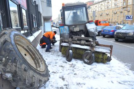 Поломка трактора для очистки тротуаров. На снимке: мужчины меняют колесо на тракторе.