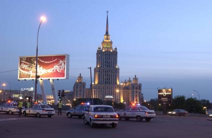 Машины ДПС едут по вечерней Москве рядом с гостиницей \"Украина\".