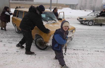 Люди толкают заглохшую машину зимой.