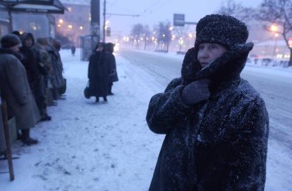 Люди на остановке во время метели в городе.