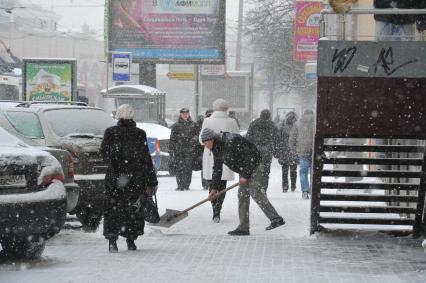 Снегопад в городе.  На снимке: гастарбайтер убирает лопатой снег с тротуара.