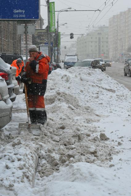 Снегопад в городе.  На снимке: мужчина убирает снег с тротуара.