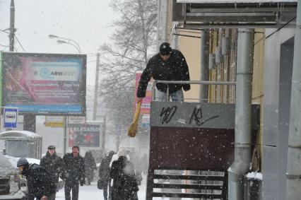 Снегопад в городе.  На снимке: мужчина счищает веником  снег с бордюра лестницы.