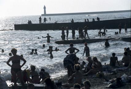 Люди на закате загорают на пляже и купаются в море.