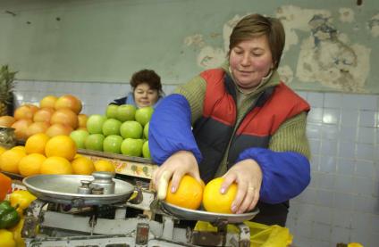 Продавщица взвешивает апельсины на рынке.