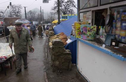 Уличная торговля в провинциальном городе. Пожилой мужчина с костылем проходи мимо палатки хозяйственными товарами.