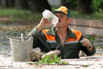 Рабочий вылез из люка и пьет воду.