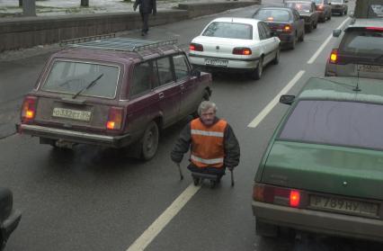 Мужчина-инвалид без ног едет на каталке против движения между машинами.