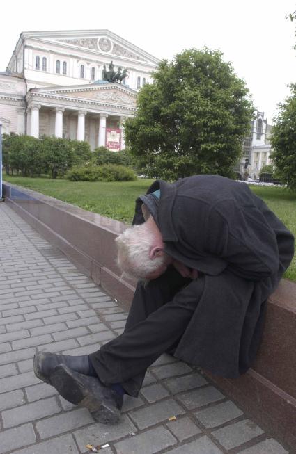 Бездомный мужчина сидит в сквере рядом с Большим театром.