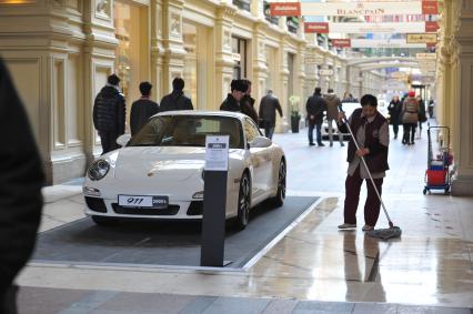 ГУМ. Выставка уникальных автомобилей Porsche, расположенных вдоль первой линии магазина, которая была временно стилизована под `Улицу Porsche`. На снимке: уборщица и автомобиль Porsche.