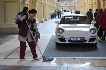 ГУМ. Выставка уникальных автомобилей Porsche, расположенных вдоль первой линии магазина, которая была временно стилизована под `Улицу Porsche`.На снимке: уборщица и автомобиль Porsche.