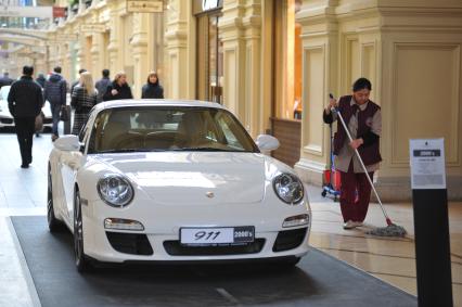 ГУМ. Выставка уникальных автомобилей Porsche, расположенных вдоль первой линии магазина, которая была временно стилизована под `Улицу Porsche`.На снимке: уборщица и автомобиль Porsche.