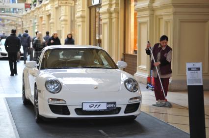 ГУМ. Выставка уникальных автомобилей Porsche, расположенных вдоль первой линии магазина, которая была временно стилизована под `Улицу Porsche`.На снимке: уборщица и автомобиль Porsche.