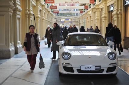 ГУМ. Выставка уникальных автомобилей Porsche, расположенных вдоль первой линии магазина, которая была временно стилизована под `Улицу Porsche`.На снимке: уборщица и автомобиль Porsche.