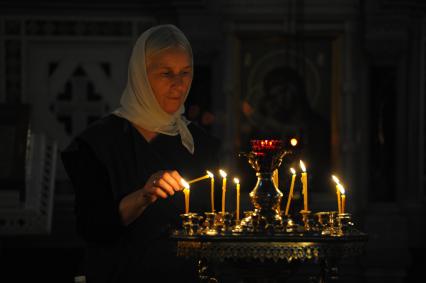 Женщина поджигает свечу в храме.