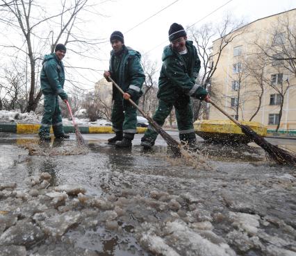 Гастарбайтеры метлой сметают лужу с дороги.