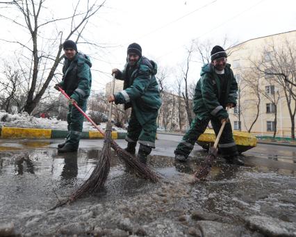 Гастарбайтеры метлой сметают лужу с дороги.