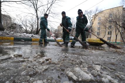 Гастарбайтеры метлой сметают лужу с дороги.