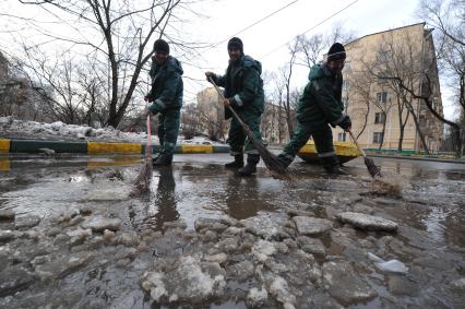 Гастарбайтеры метлой сметают лужу с дороги.