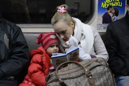 Мать дочери  читает книгу во время поездки в метро.