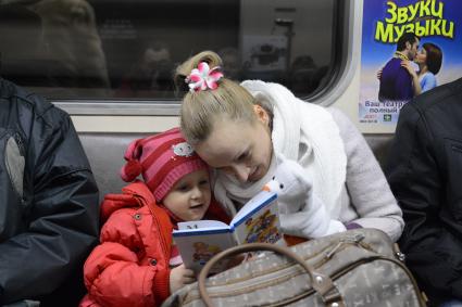 Мать дочери  читает книгу во время поездки в метро.