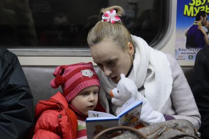 Мать дочери  читает книгу во время поездки в метро.