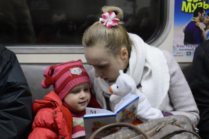 Мать дочери  читает книгу во время поездки в метро.