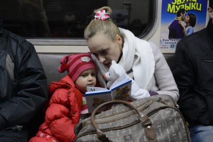 Мать дочери  читает книгу во время поездки в метро.