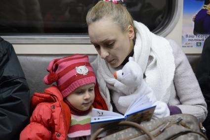 Мать дочери  читает книгу во время поездки в метро.