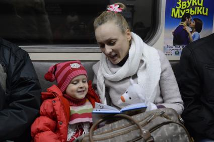 Мать дочери  читает книгу во время поездки в метро.