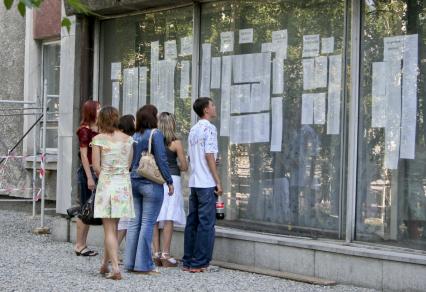 Абитуриенты ищут свои фамили в списках людей сдававших экзамены.