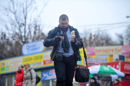 Молодой человек идет по улице с телефоном и шаурмой в руках.