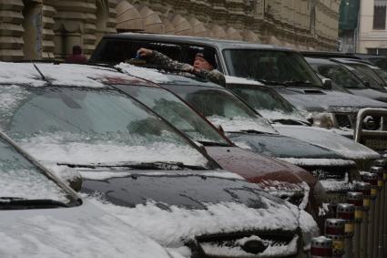 Мегаполис. Автомобильная парковка. На снимке: мужчина счищает снег с автомобиля.