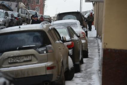 Припаркованные автомобили и пешеходы на городской улице.