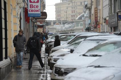 Припаркованные автомобили и пешеходы на городской улице.