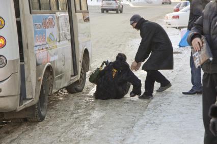 Женщина упала при выходе из автобуса, мужчина подходит к ней чтобы помочь подняться.