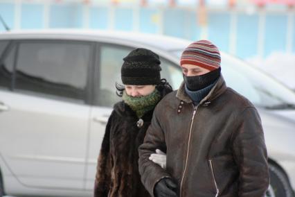 Пара мужчина и женщина идут под руку. Мужчина вжимается в куртку от холода.