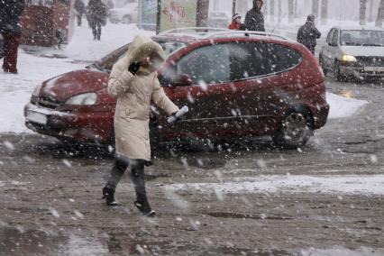 Девушка в снегопад переходит дорогу с оживленным движением.