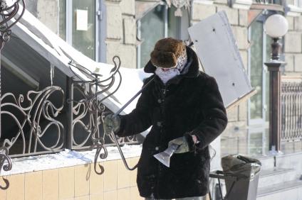 Замерзший дворник с лопатой и ледорубом идет по улице.