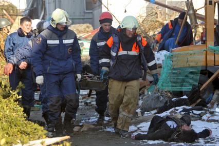 Спасатели несут на носилках тело погибшего человека, на дороге лежит еще одна жертва стихии.