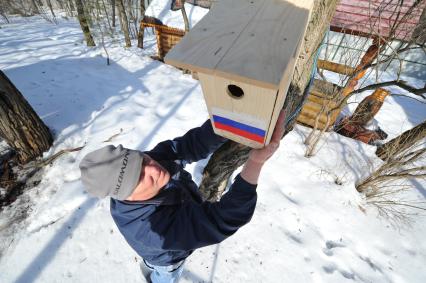 Мужчина вешает скворечник на дерево.