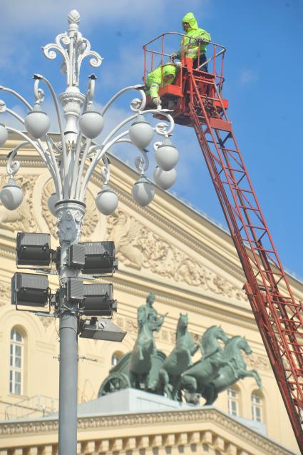 Гастарбайтеры красят фонарь перед зданием большого театра.