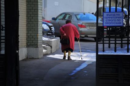 Пенсионерка с палочкой идет по двору дома.