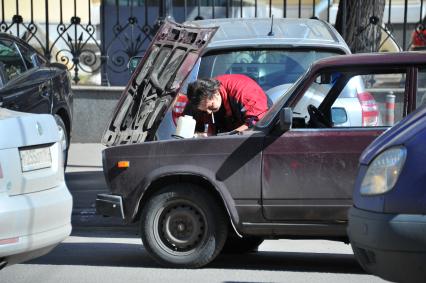 Мужчина ремонтирует автомобиль на дороге.