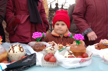 Ребенок стоит около стола с куличами.