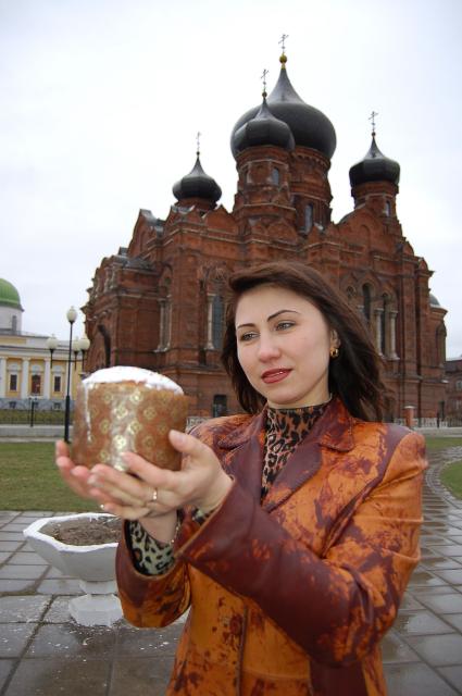 Девушка стоит на фоне здания церкви, держит в руках пасхальный кулич.