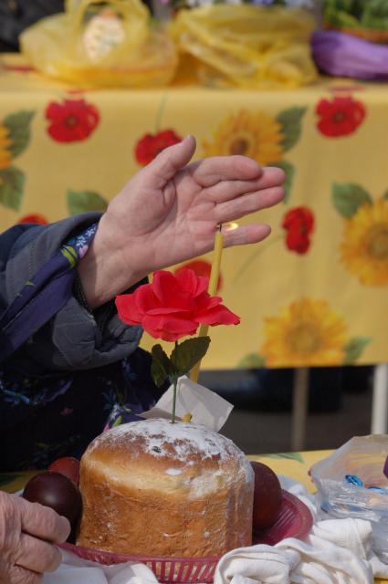 Женская рука оберегает свечку в праздничном пасхальном куличе от затухания на ветру.