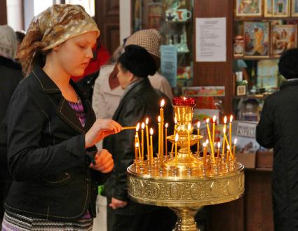 Девушка в церкви ставит свечку в подсвечник.