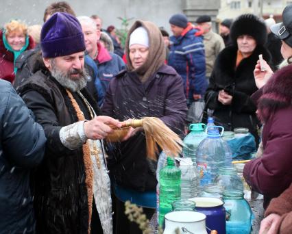 На улице священник освящает емкости (бутылки банки) с водой обрызгивая кропилом.